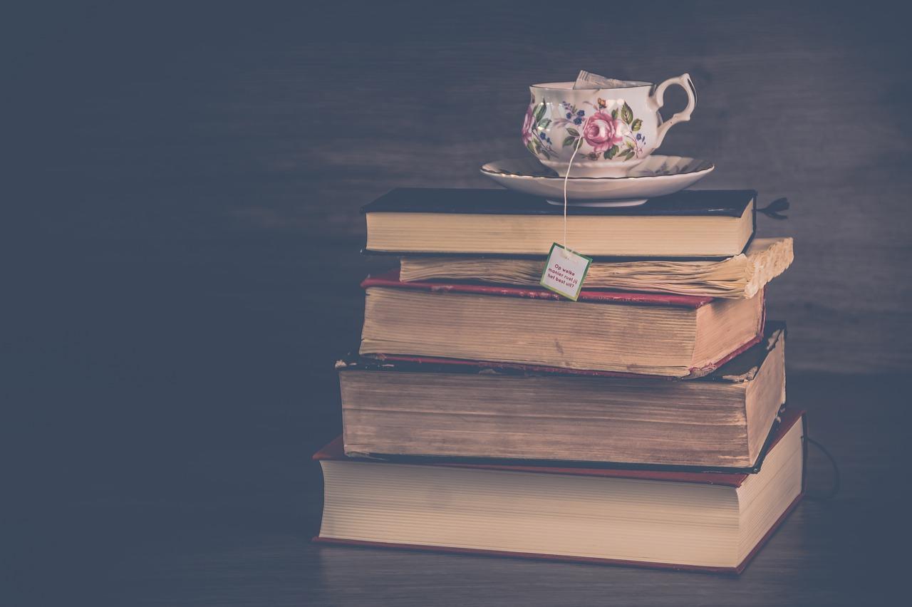 A pile of old books with a teacup perched on top.