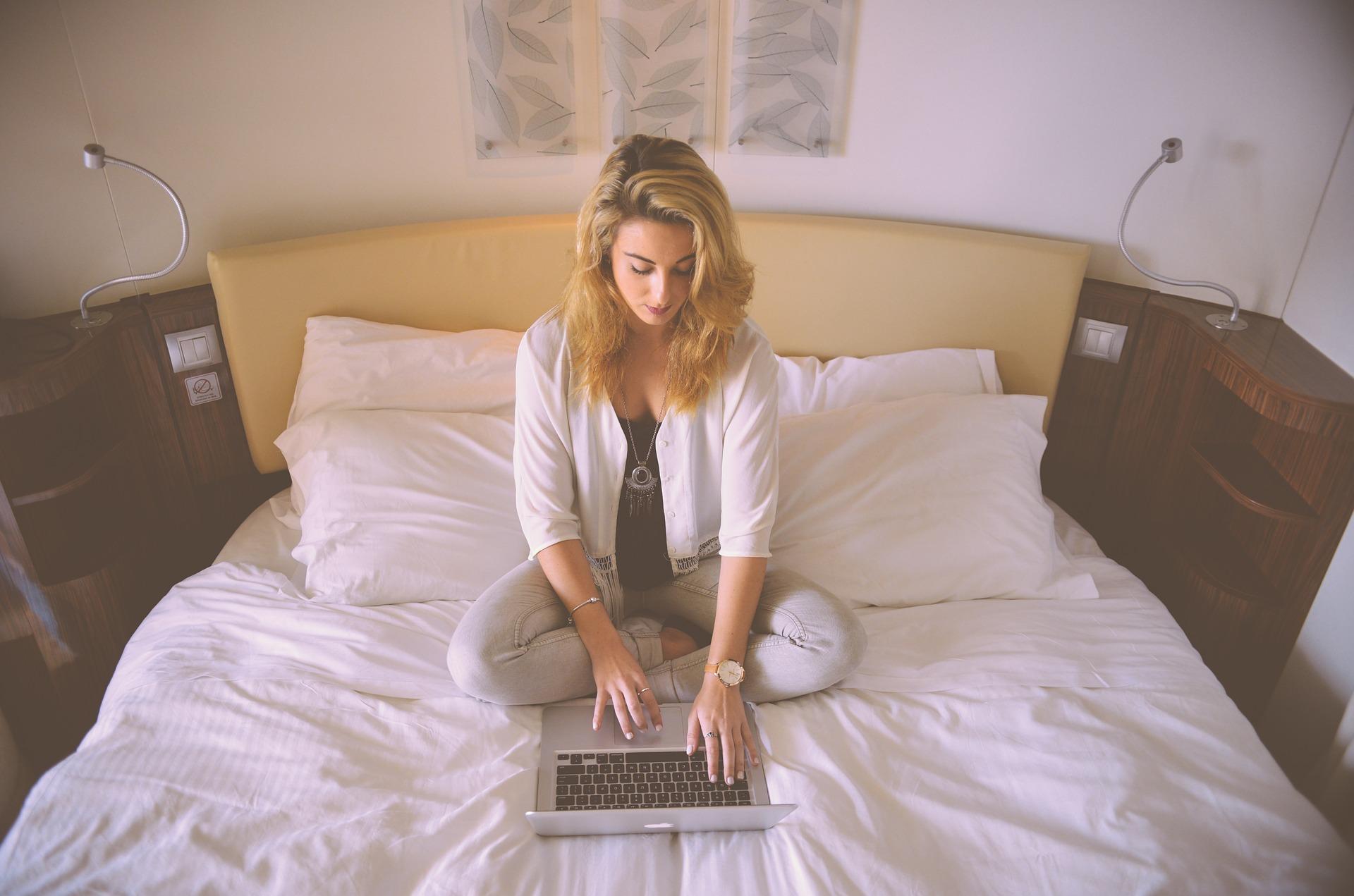 woman sitting on a bed working on a laptop