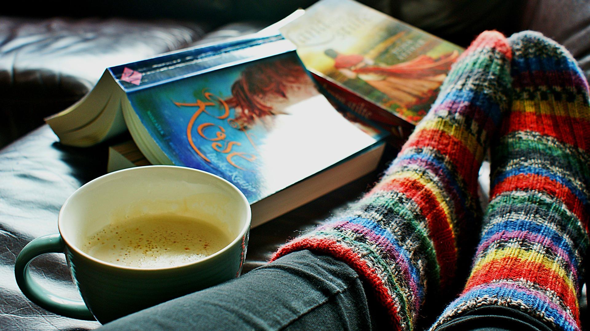 some feet with woolen socks by a cup of coffee and a book