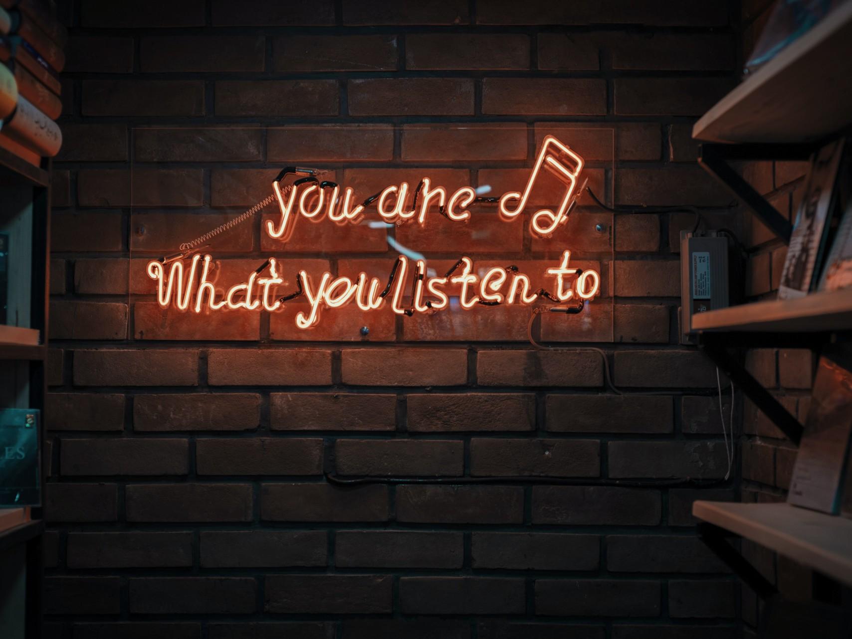 Neon lights reading, "you are what you listen to", against brick wall 