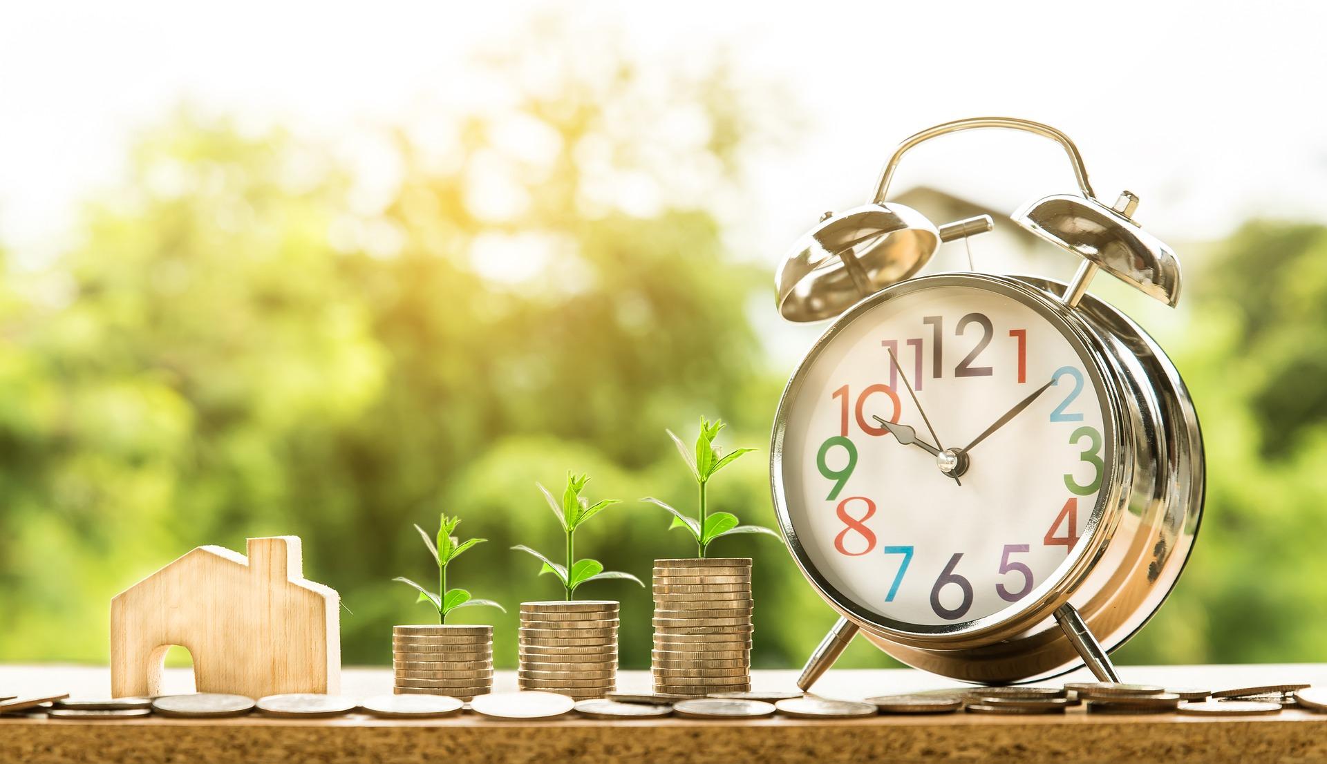 A small wooden house, three stacks of coins and an alarm clock.