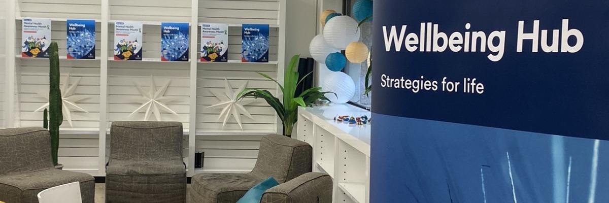 Photo of Wellbeing Hub banner, soft light brown chairs, posters, coloured lanterns and 2 plastic chairs