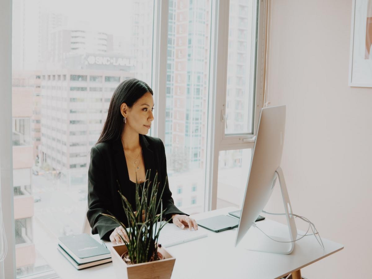 Suited person in an office sitting at a desk looking at a computer screen