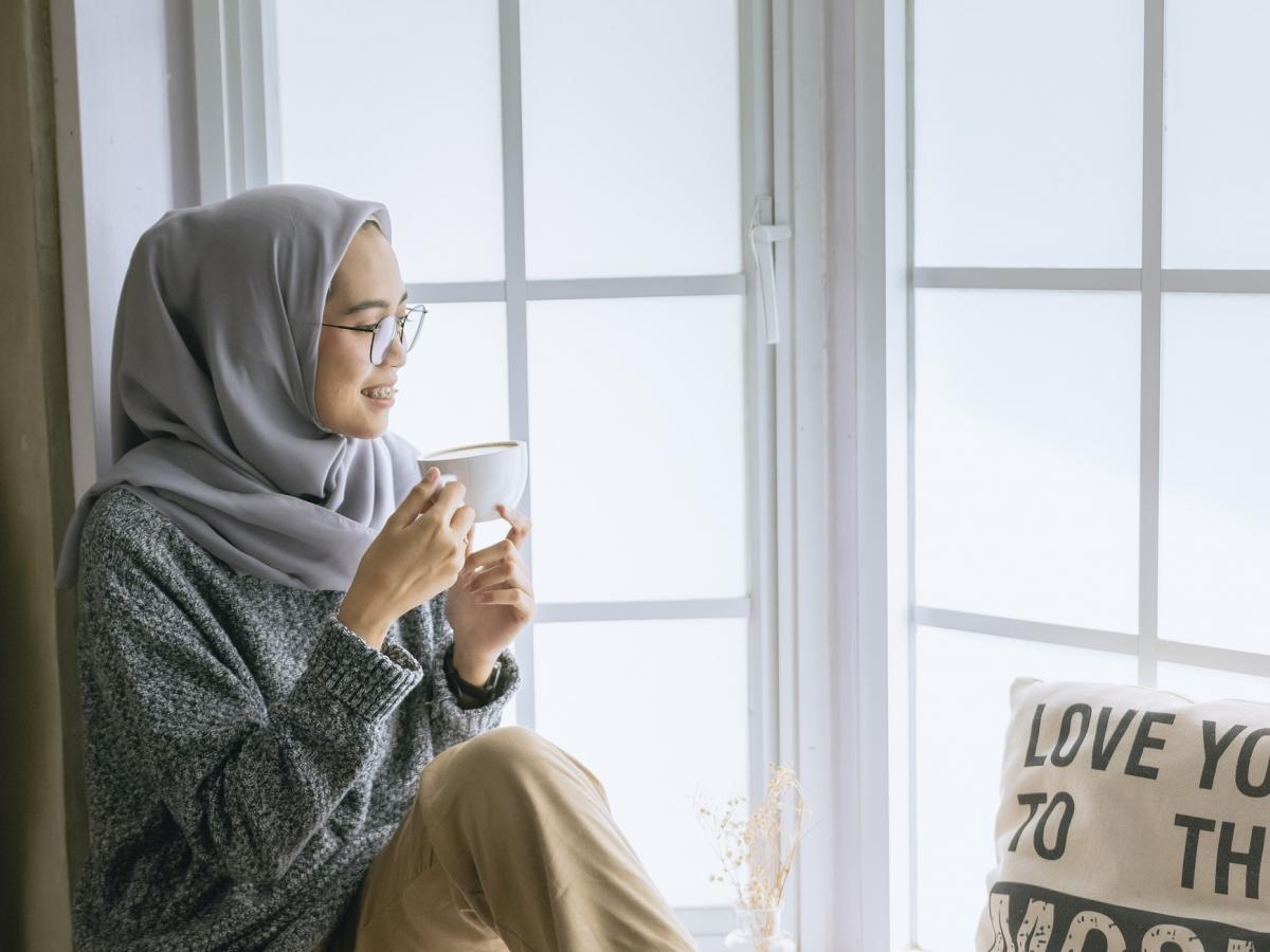 Women sitting in a window sill drinking a cup of tea and looking out the window smiling