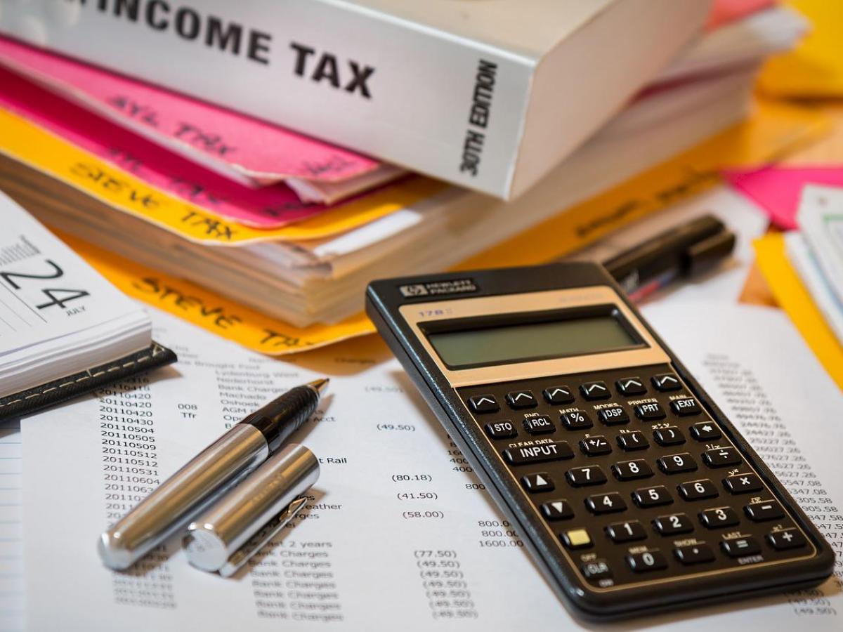 A calculator, pen, and folders sit on top of a pile of papers.
