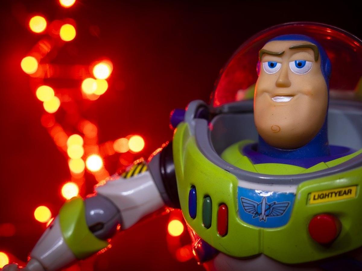 A Buzz Lightyear figurine dressed in green and purple, in front of a lit up background.