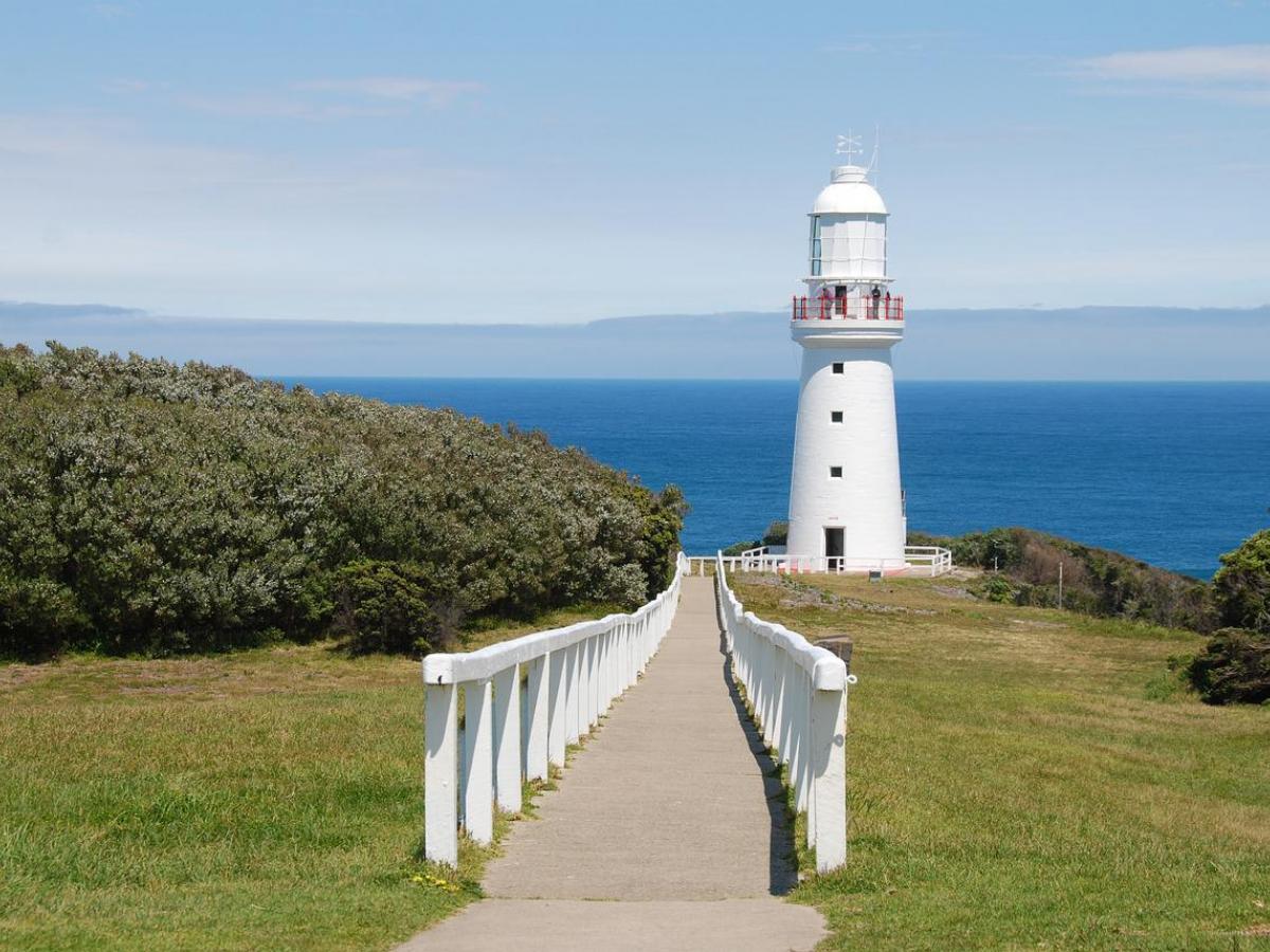 A white path leading up to a lighthouse, with the ocean behind it.