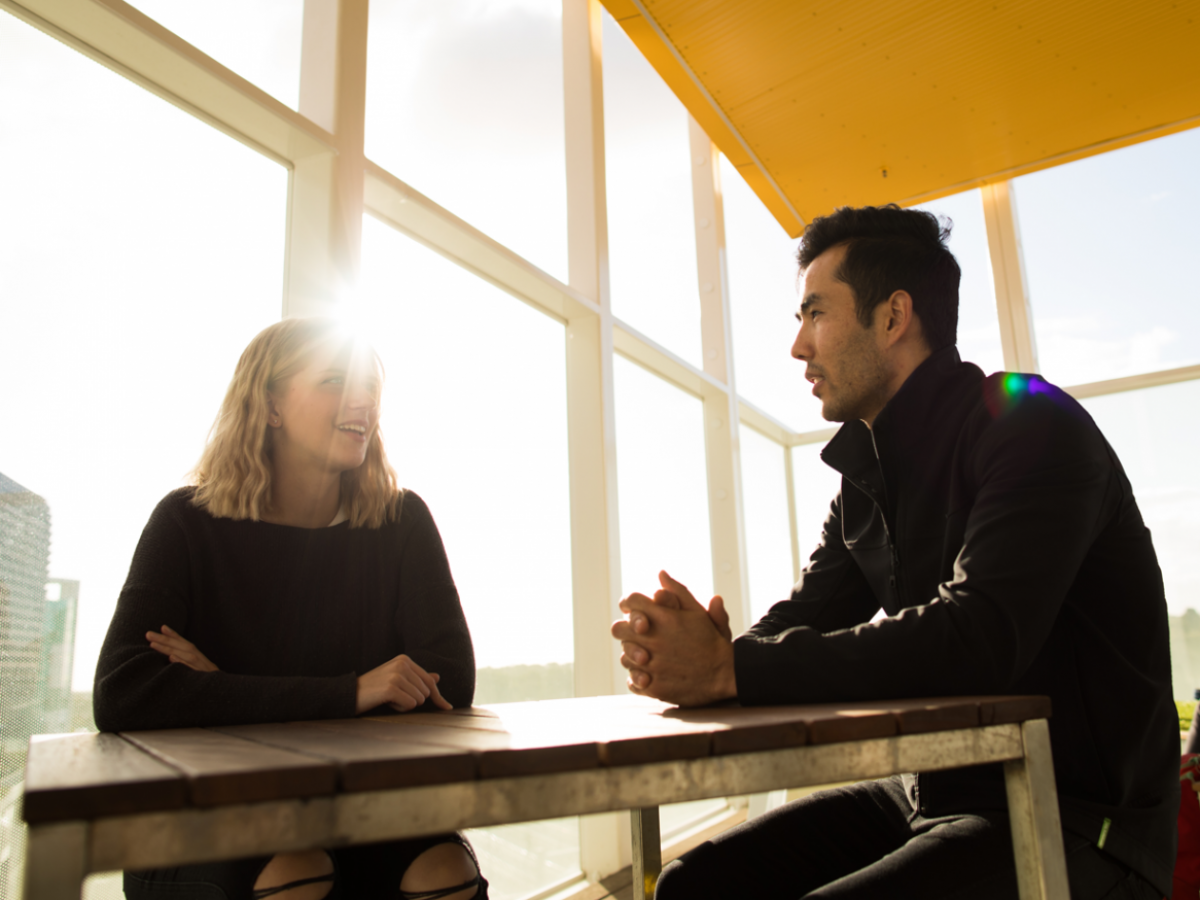 2 people sitting talking in front of a large window