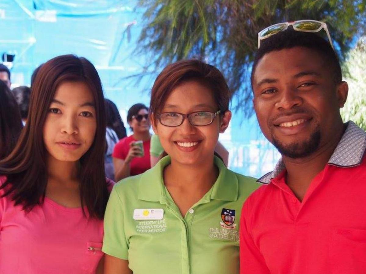 Photo of 3 people smiling at the camera wearing red, pink and green tshirts respectively