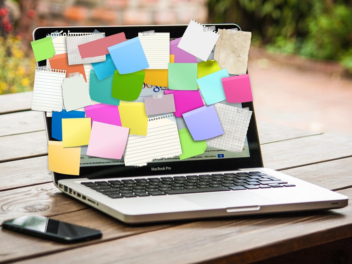 A laptop and phone are placed atop a park bench with sticky notes fully covering the laptop screen.