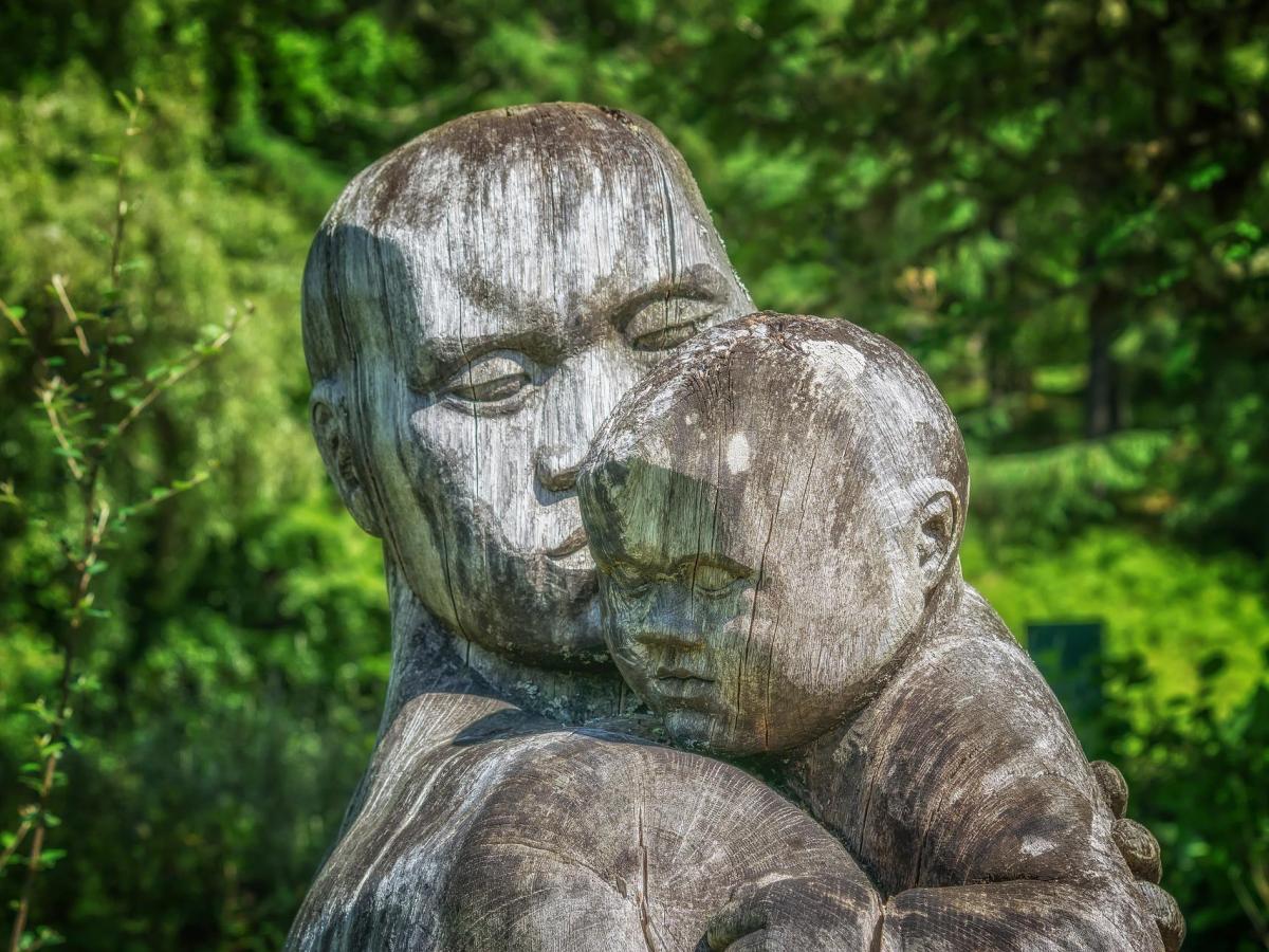 Wooden sculpture of an adult nursing a baby