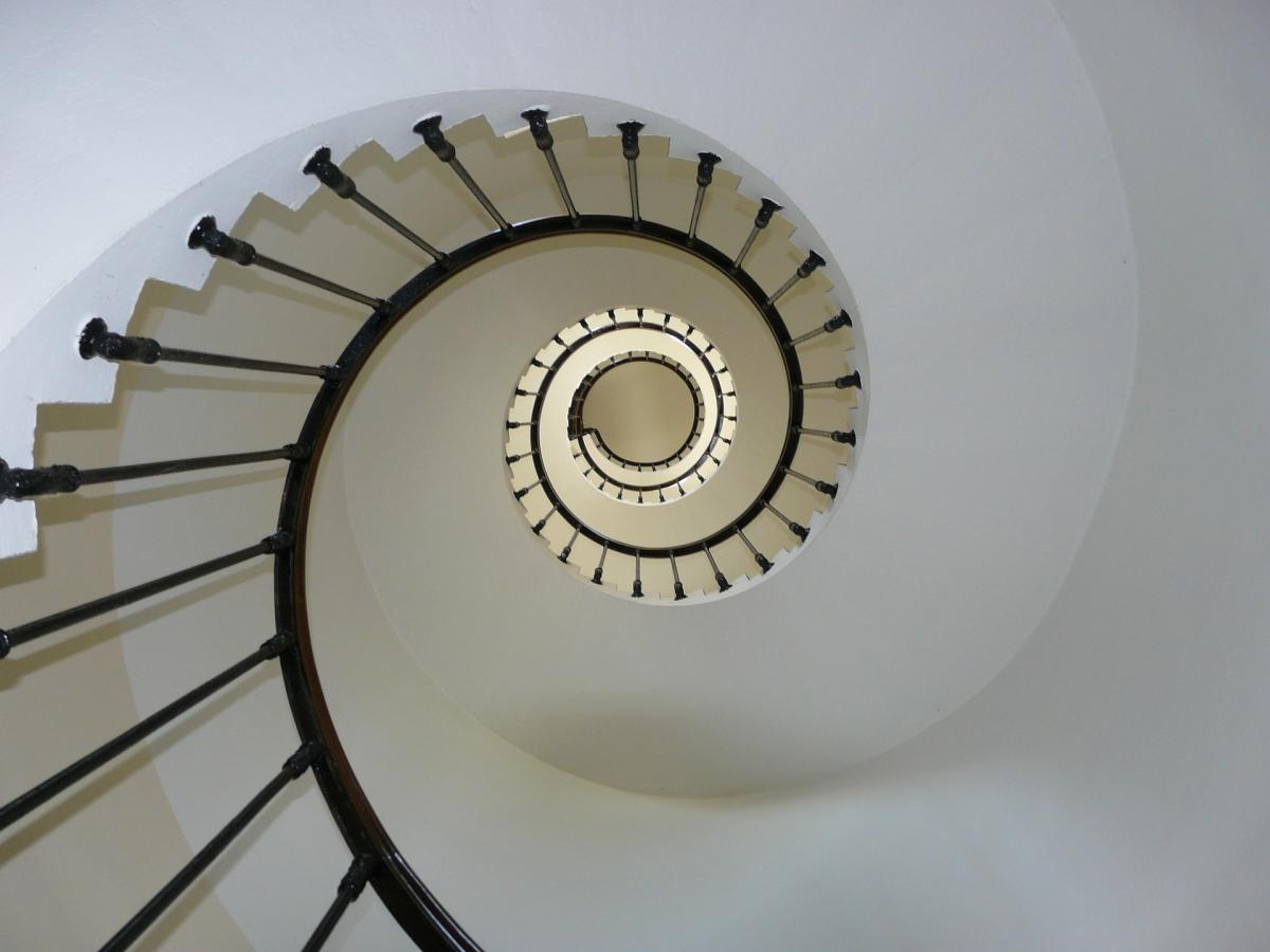 Looking at a white spiral stairway with dark wood railings from below.