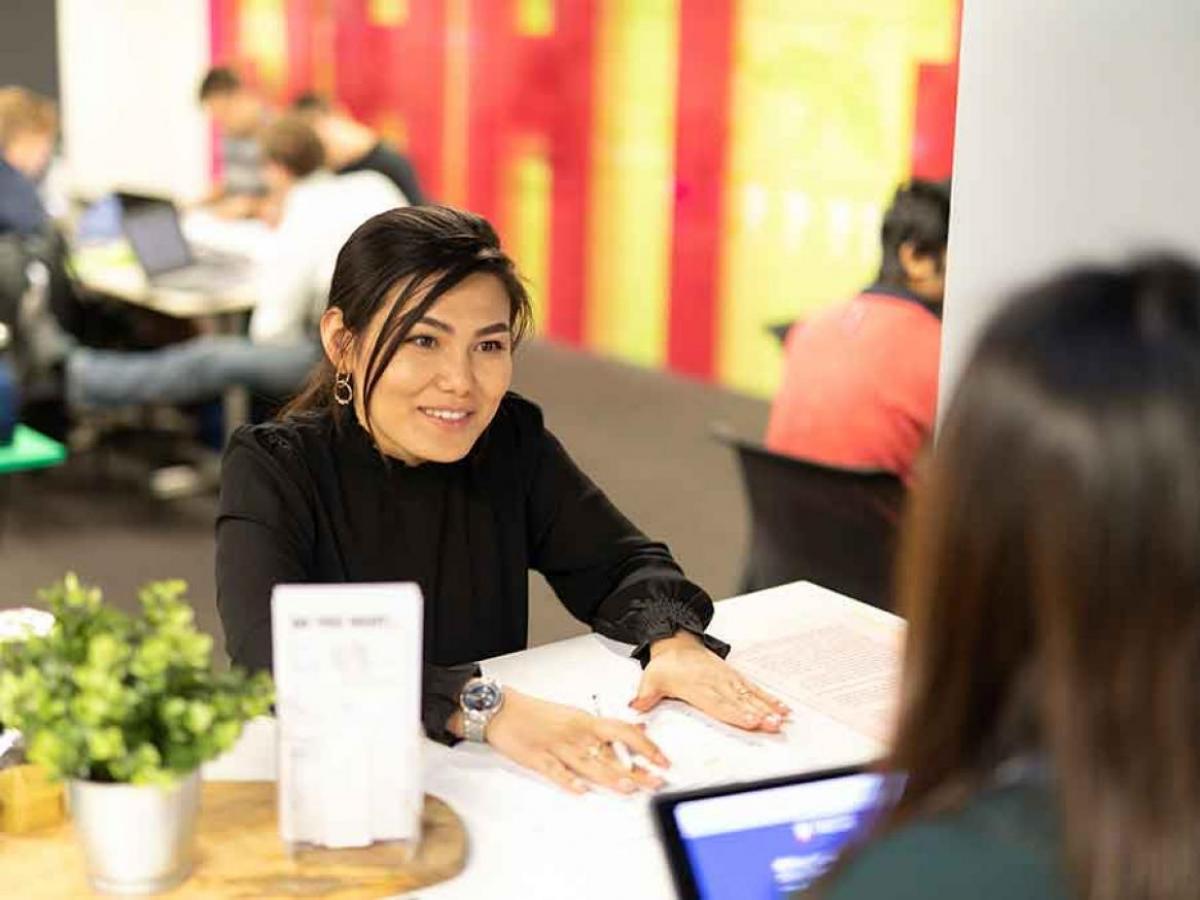 Writing Centre advisor smiling whilst sitting at desk and facing a student