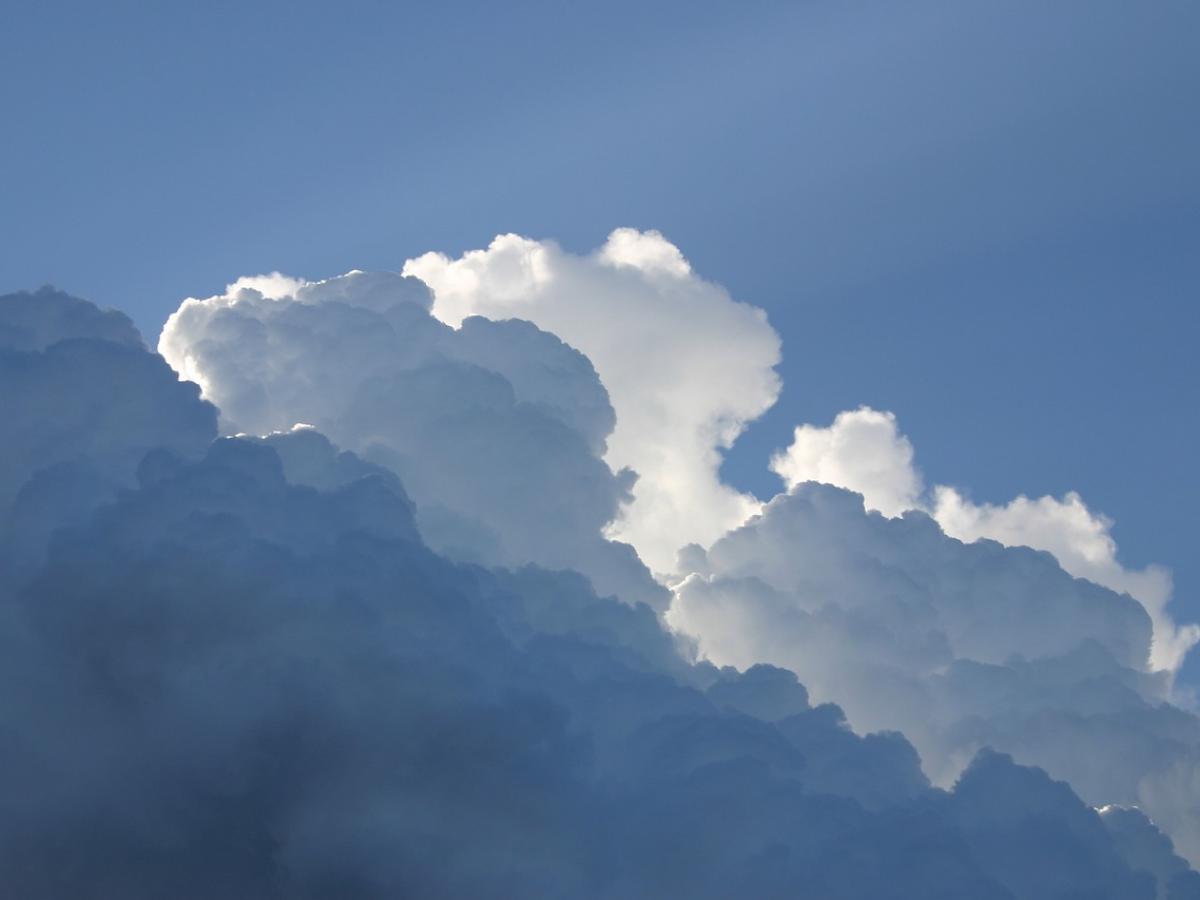 A blue sky with fluffy white back-lit clouds, and rays of sunshine streaming through.