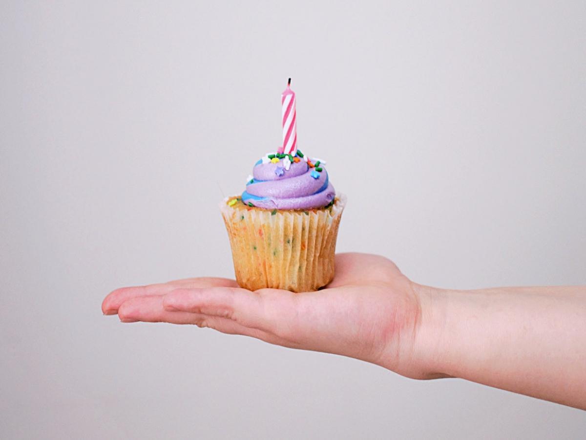 A person holding a birthday cupcake.