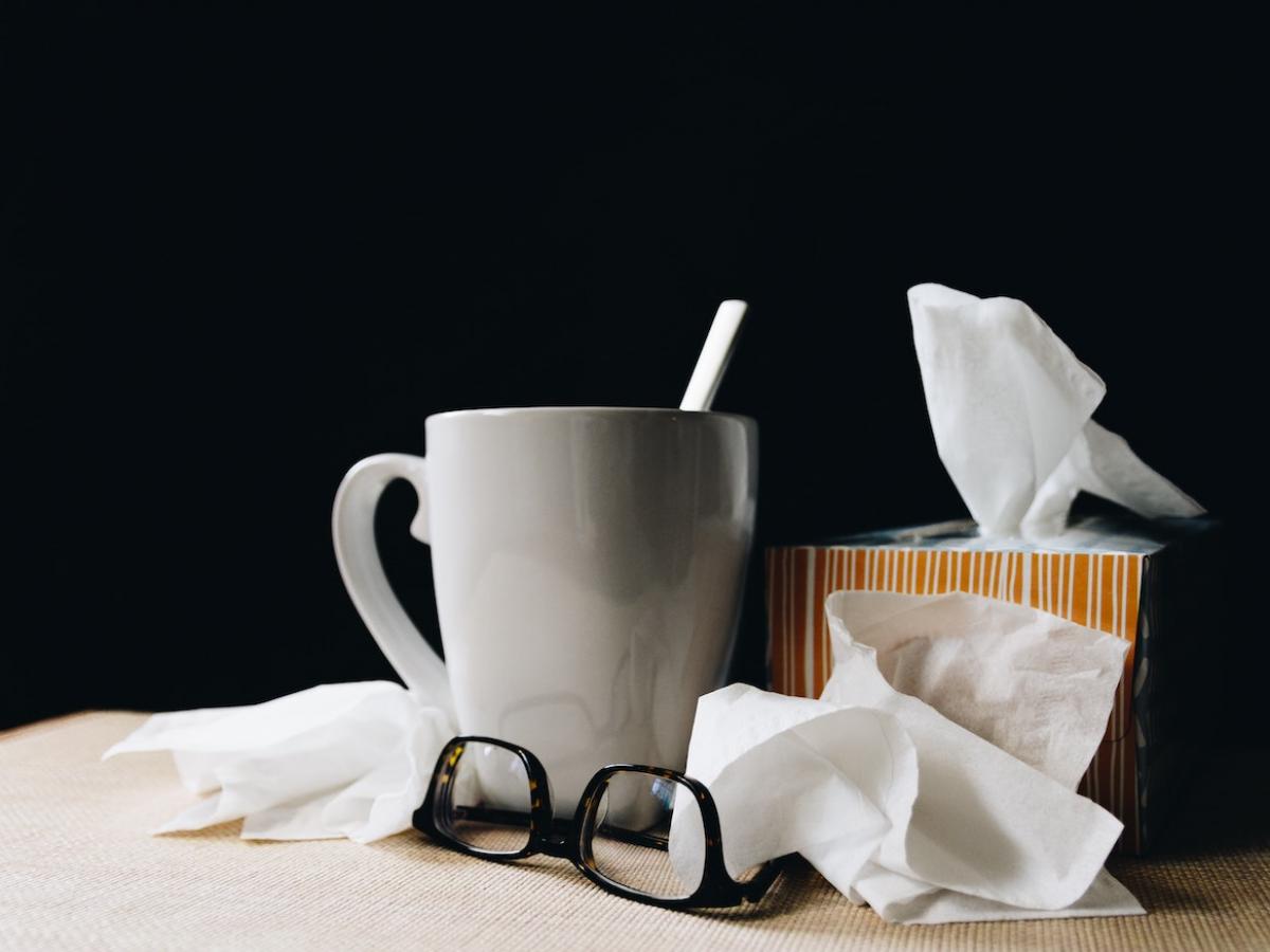 a mug, box of tissues and glasses on a desk.