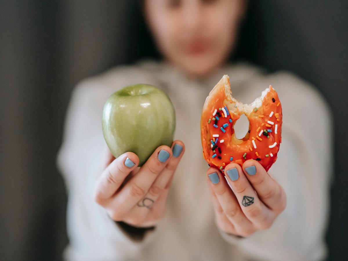 A woman holding an apple in one hand and a donut in the other