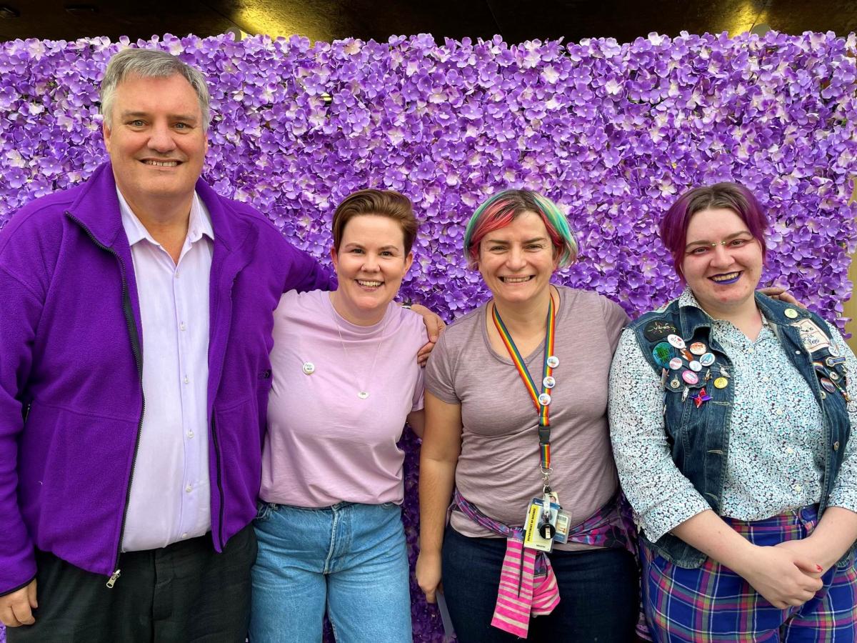 4 ALLY members standing in front of a purple flower wall
