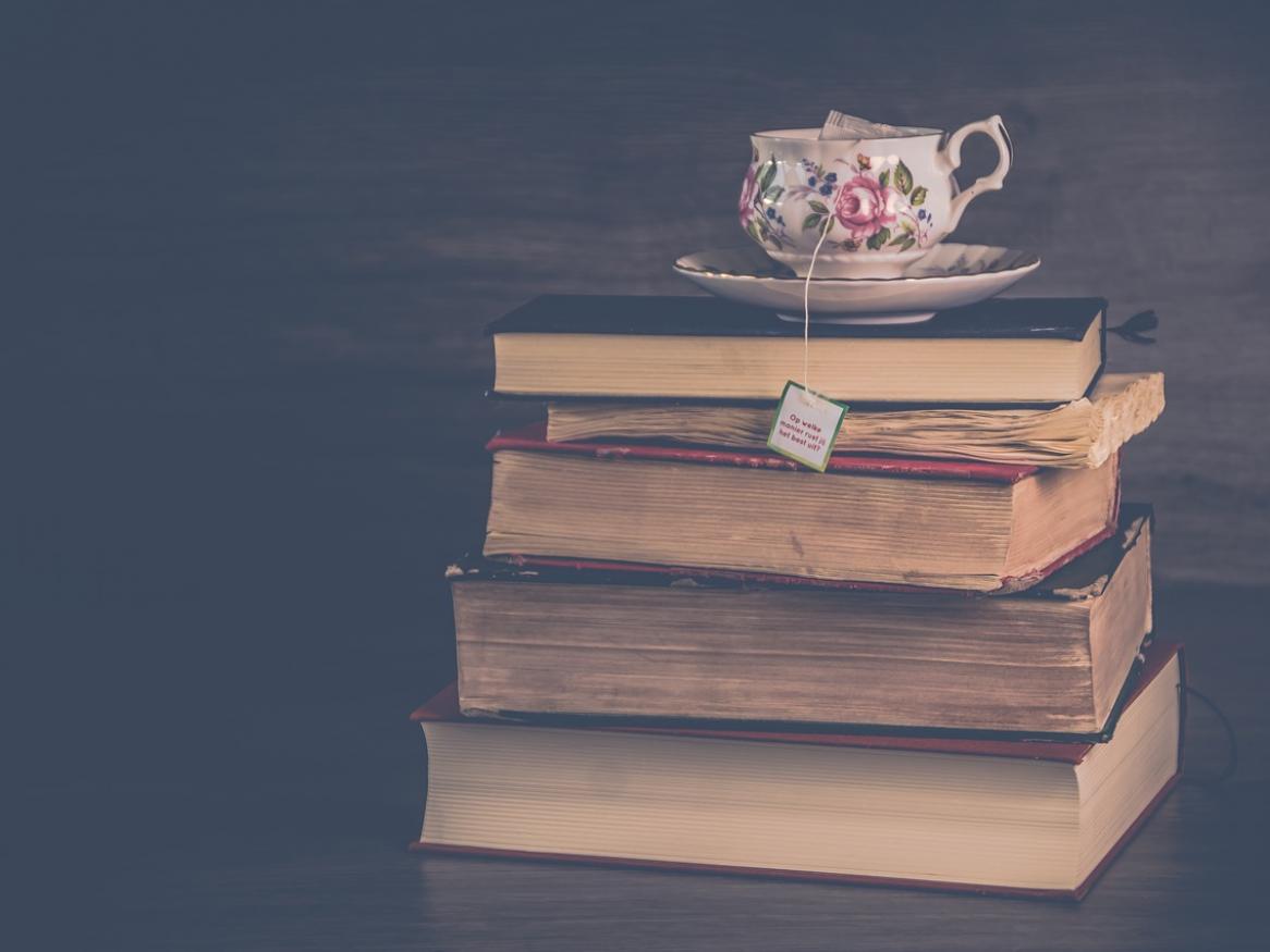 A pile of old books with a teacup perched on top. 