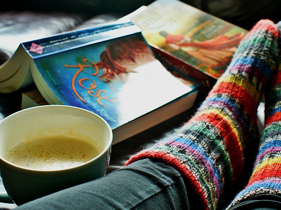 some feet with woolen socks by a cup of coffee and a book