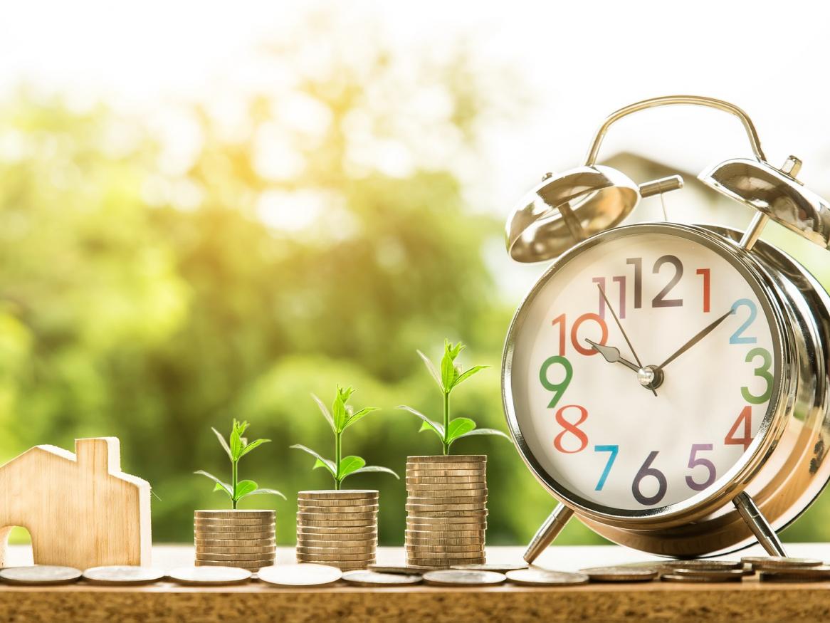 A small wooden house, three stacks of coins and an alarm clock.