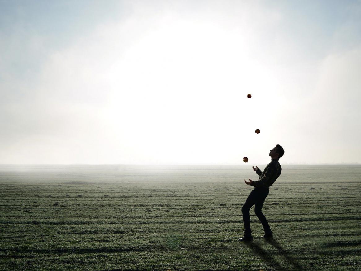 The silhouette of a man on a beach juggling three balls