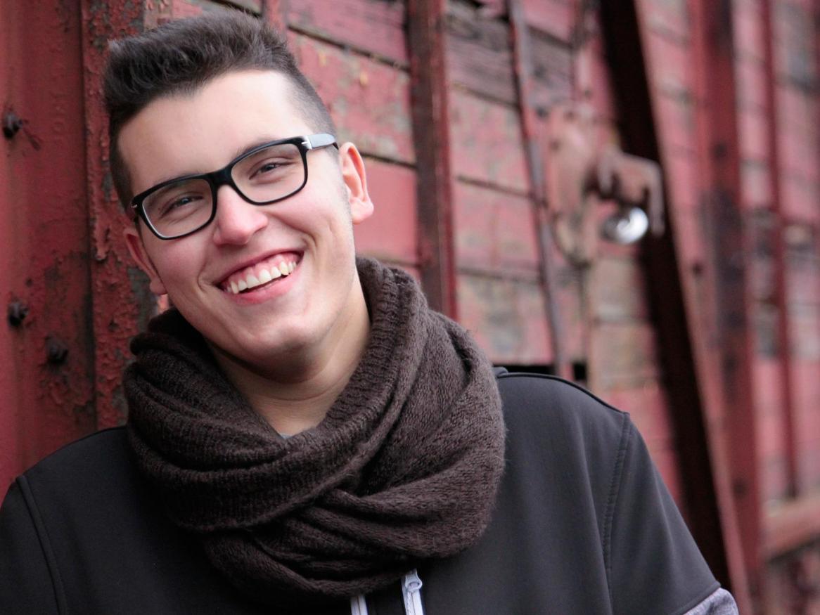 Person looking at the camera, laughing and leaning up against a wooden wall.