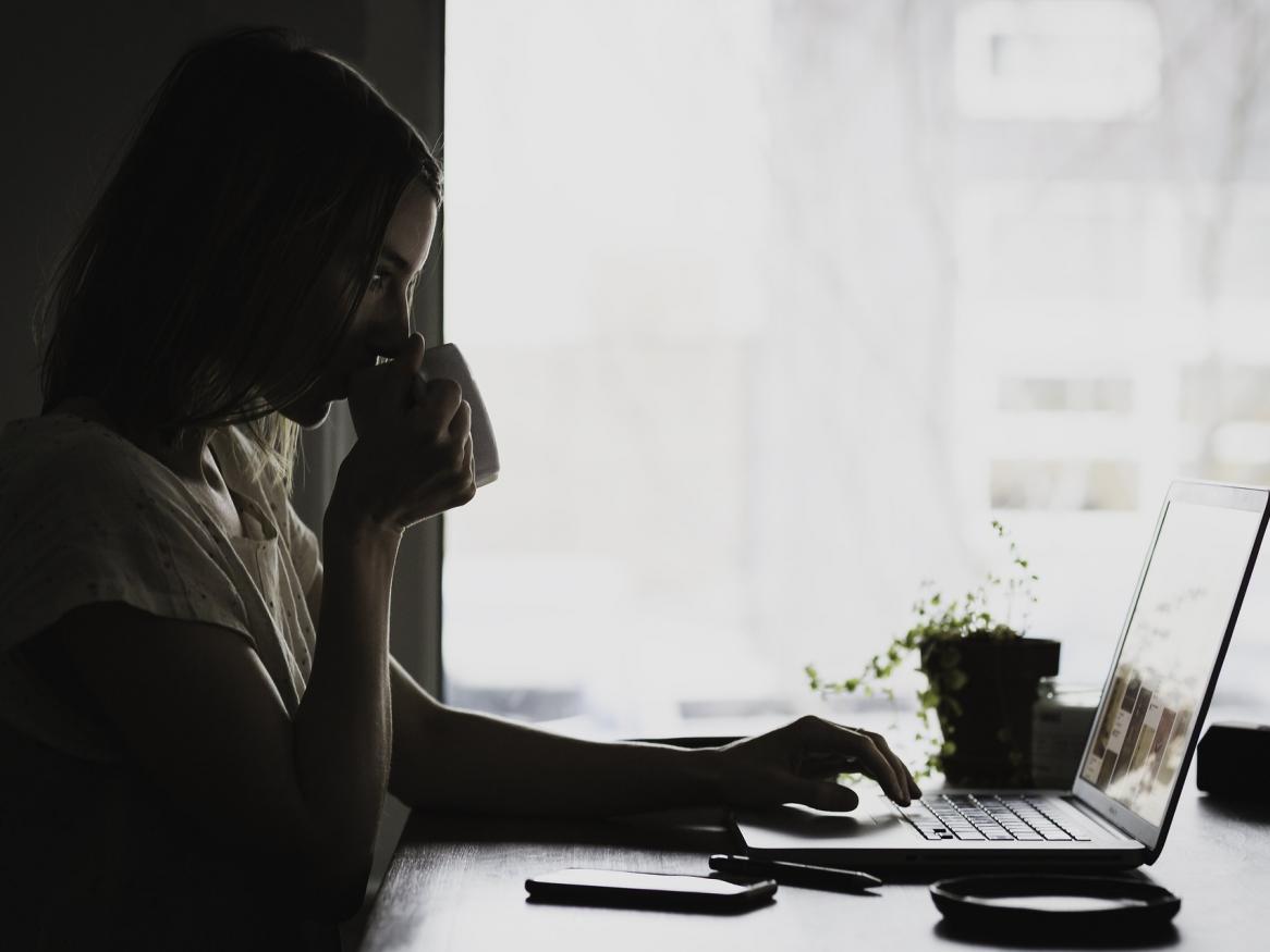 An image of woman in the dark drinking from a mug and using her laptop