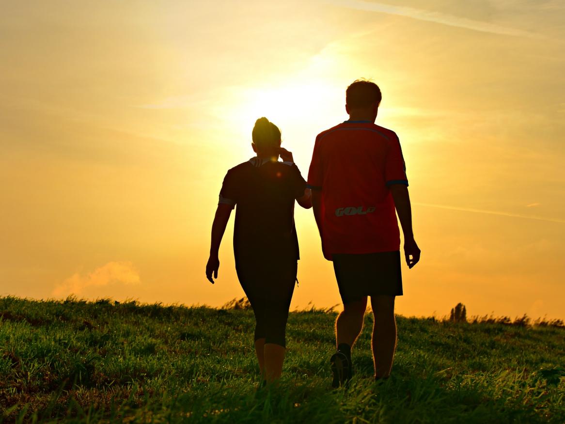 2 people walking on grass towards sun low in the sky