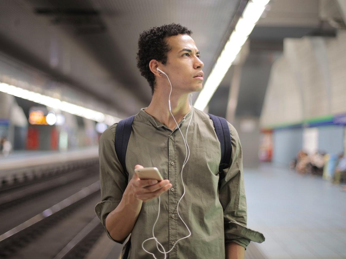 Young male holding his phone with earphones in at a train station