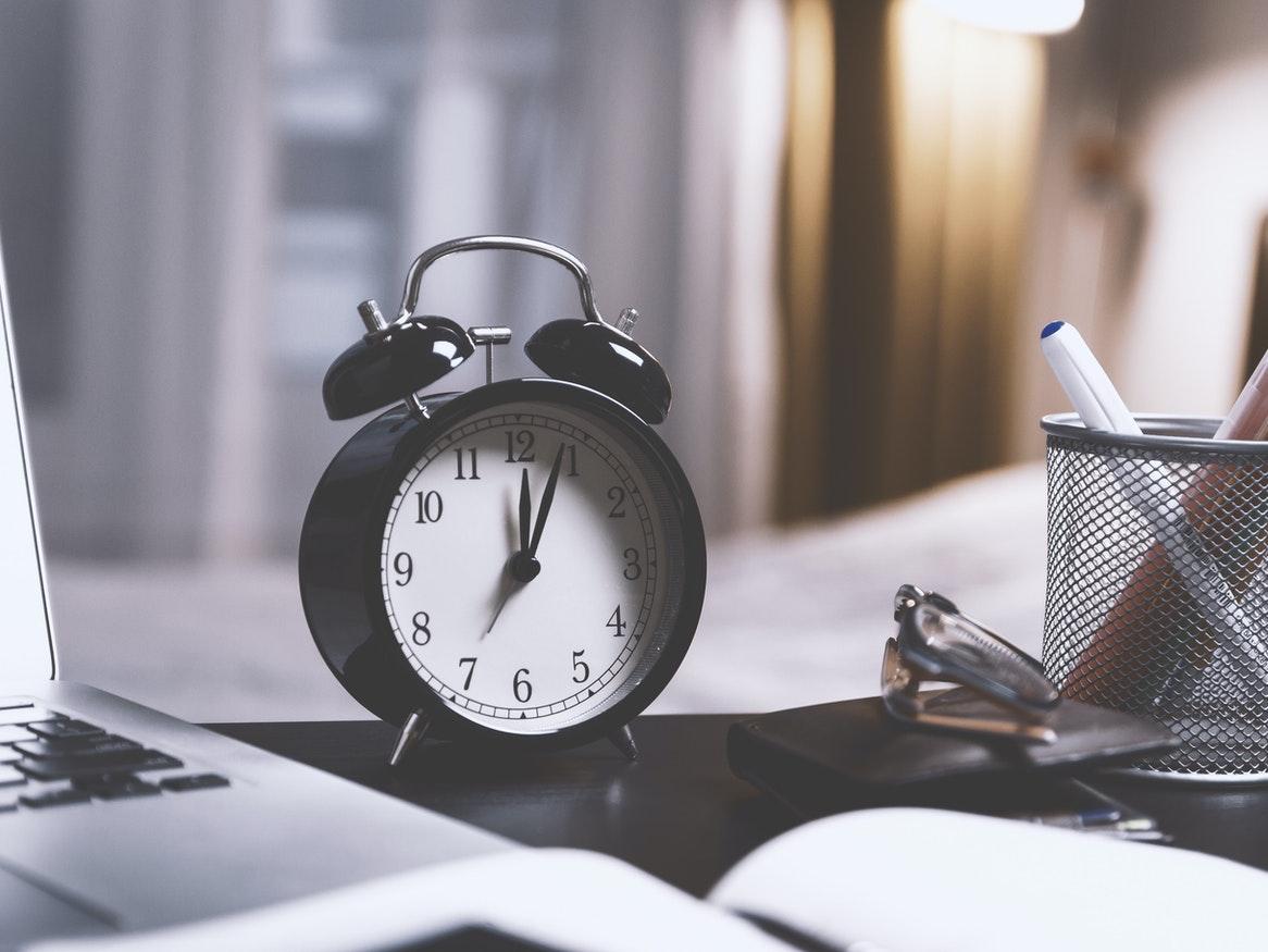 black analogue clock sitting on a desk next to a laptop