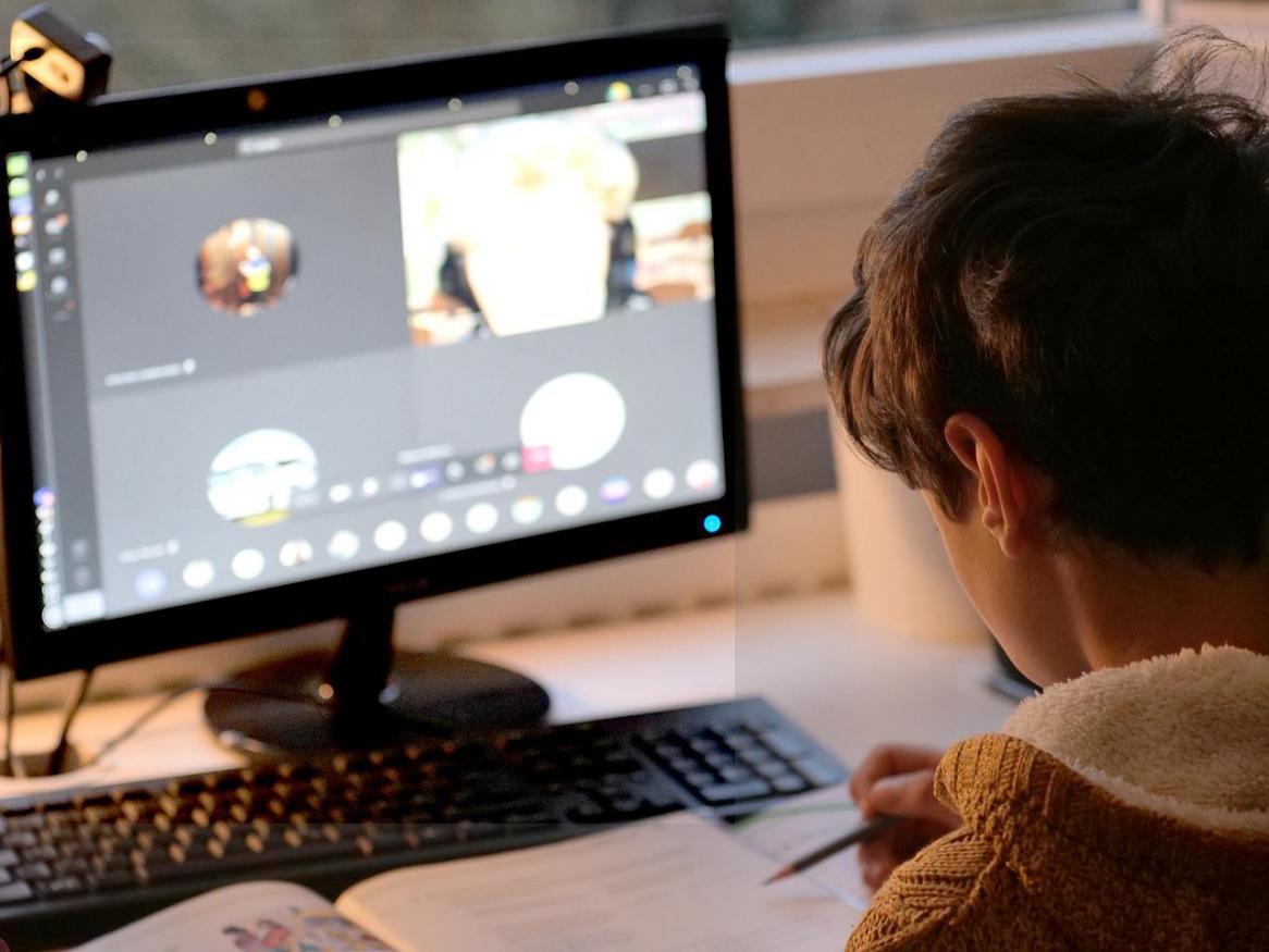 A person sits at their laptop screen, which shows four people video calling.