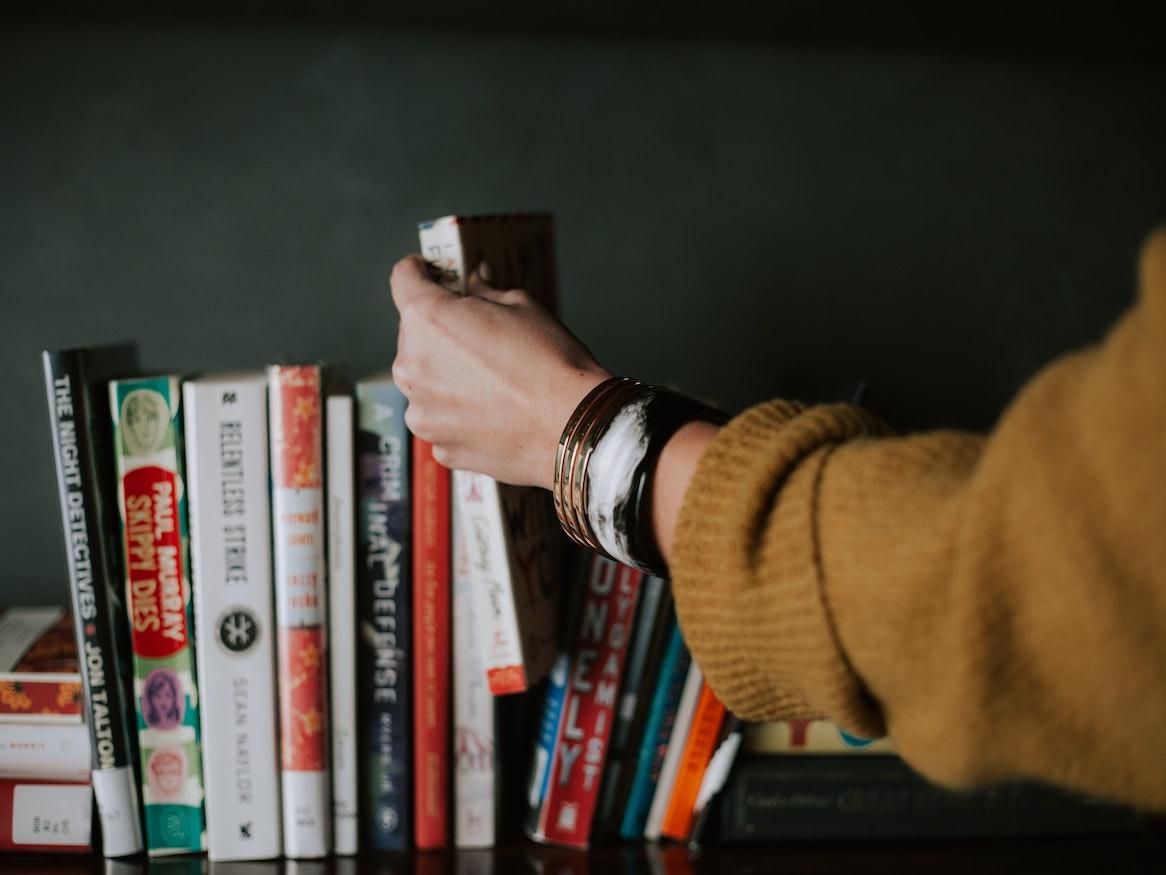 A person picking out a book from the shelf.