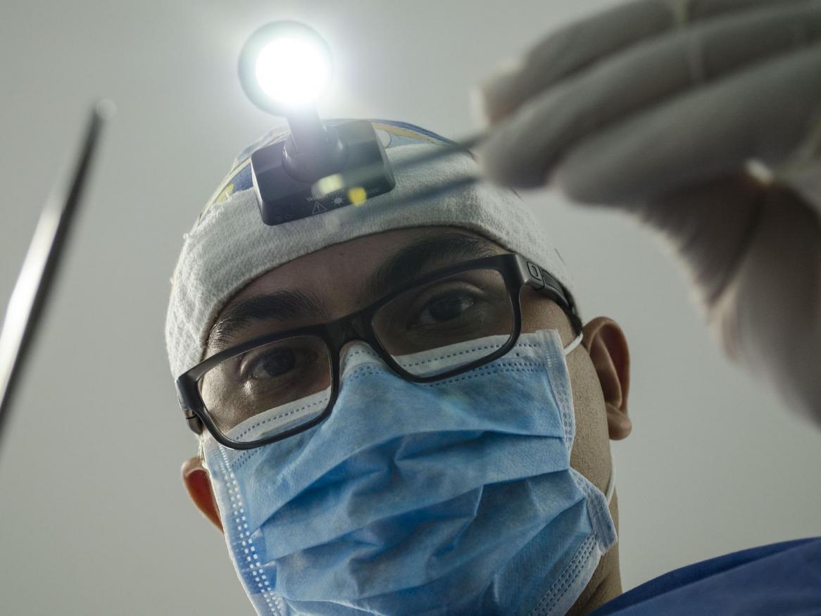 First person perspective as a patient with a dentist holding tweezers and a metal stick with a light overhead