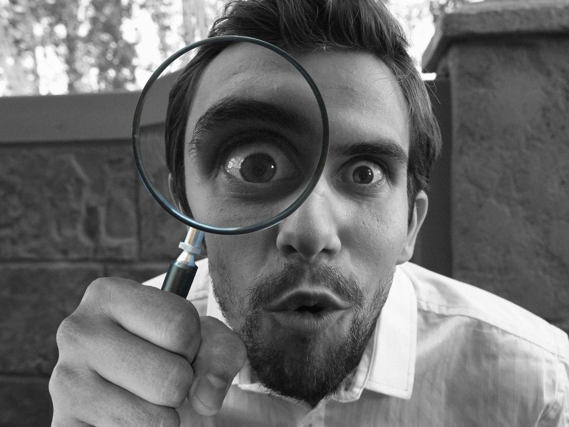 man looking through magnifying glass with one eye towards camera