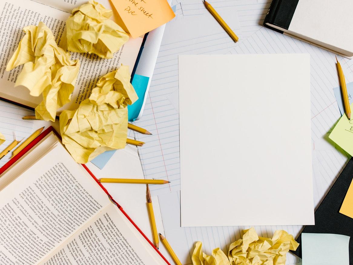 Open books, scrunched paper and pencils scattered on a desk