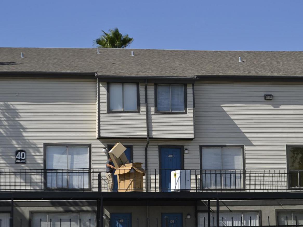 A person is moving boxes and a washing machine on an apartment balcony