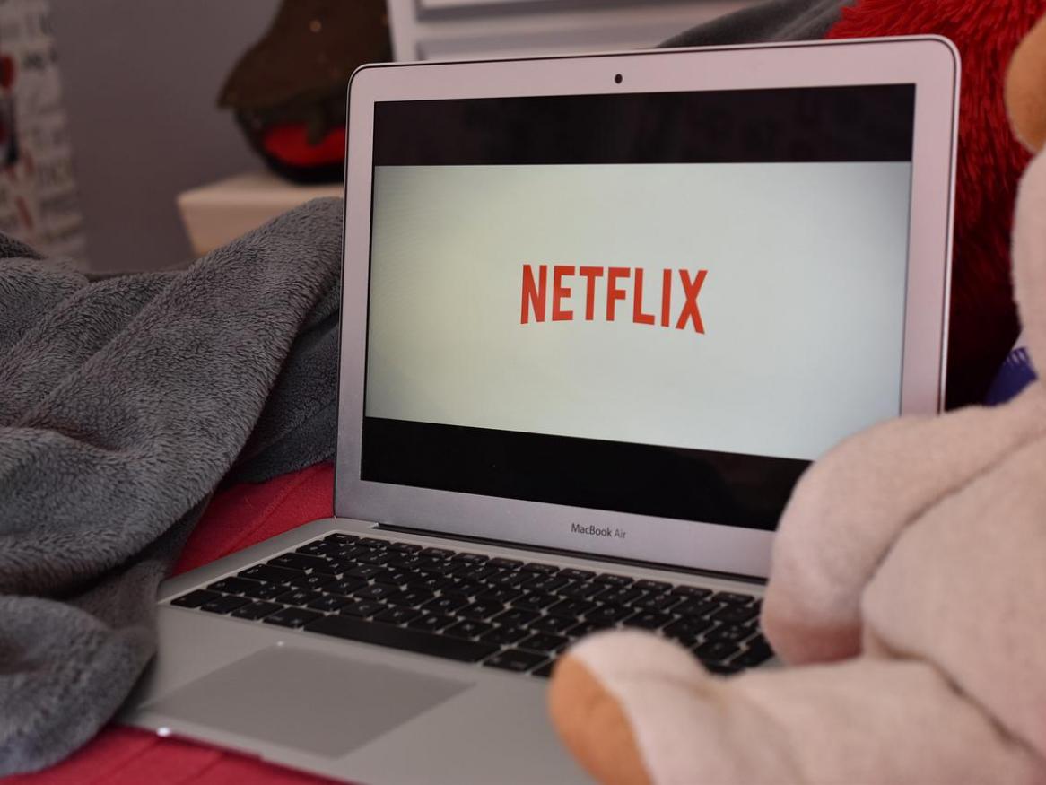 A laptop sits on a bed, with Netflix open.
