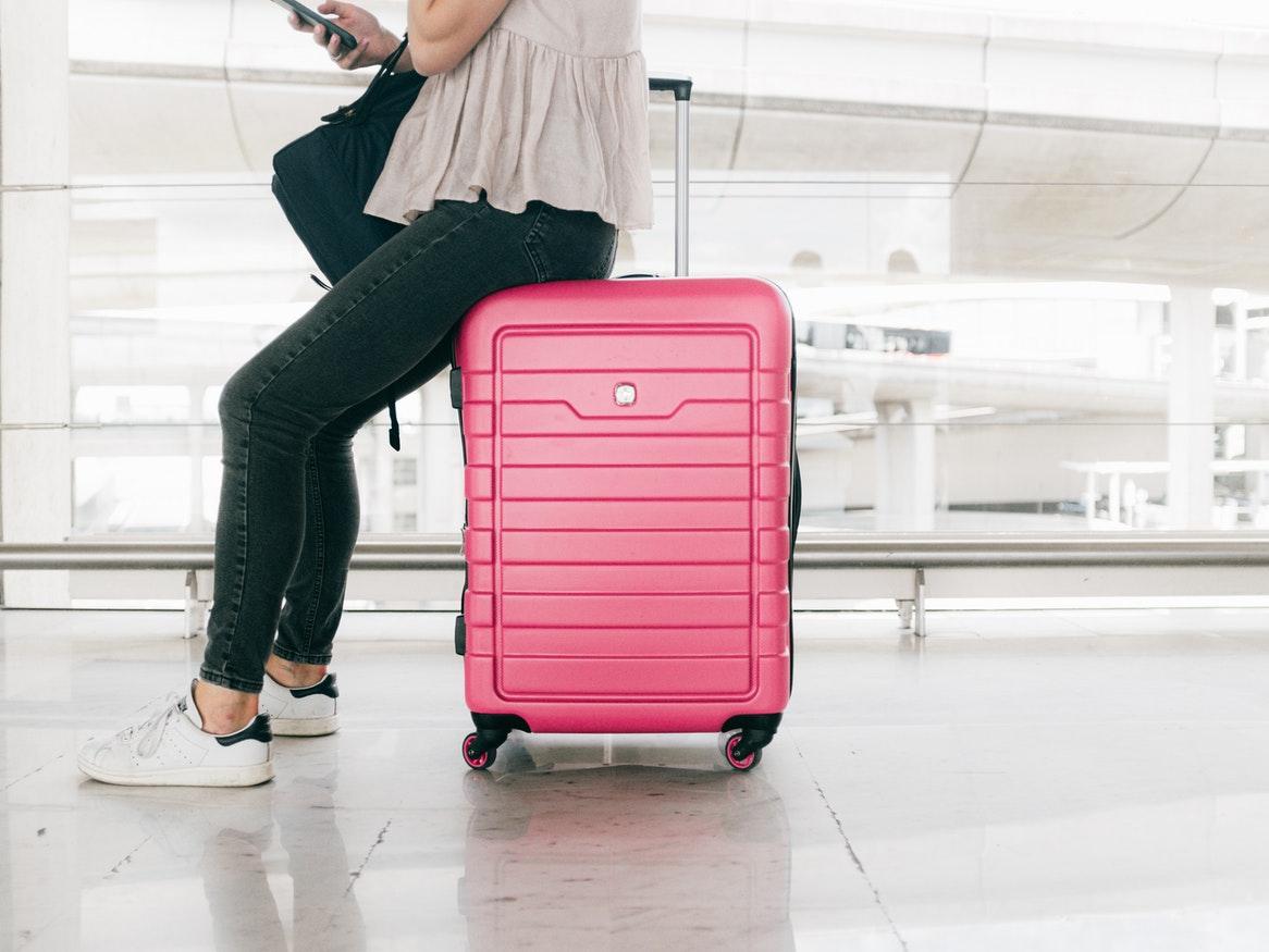 Girl sitting on a pink suitcase in an airport