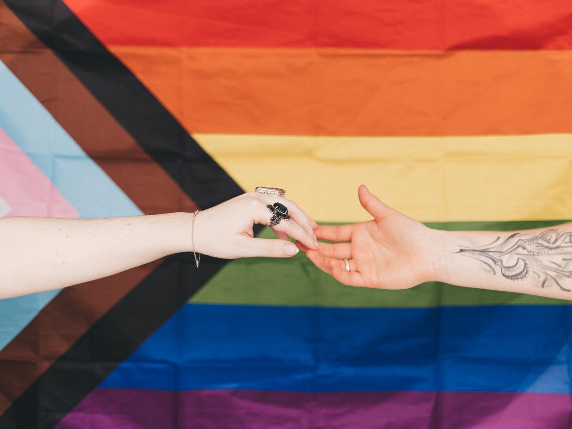 Two hands touching in front of an lgbtqia flag