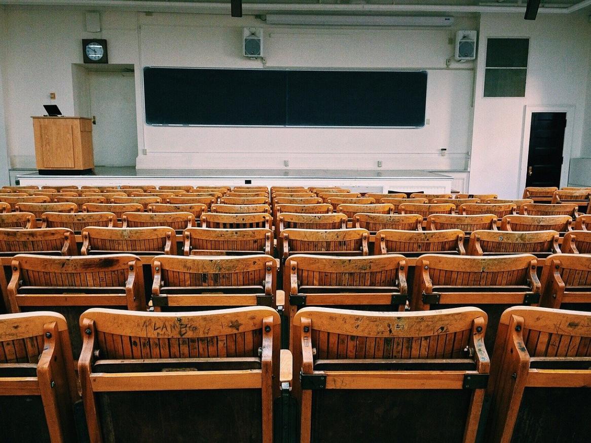 A group of empty chairs in a classroom, facing a screen and a lecture.
