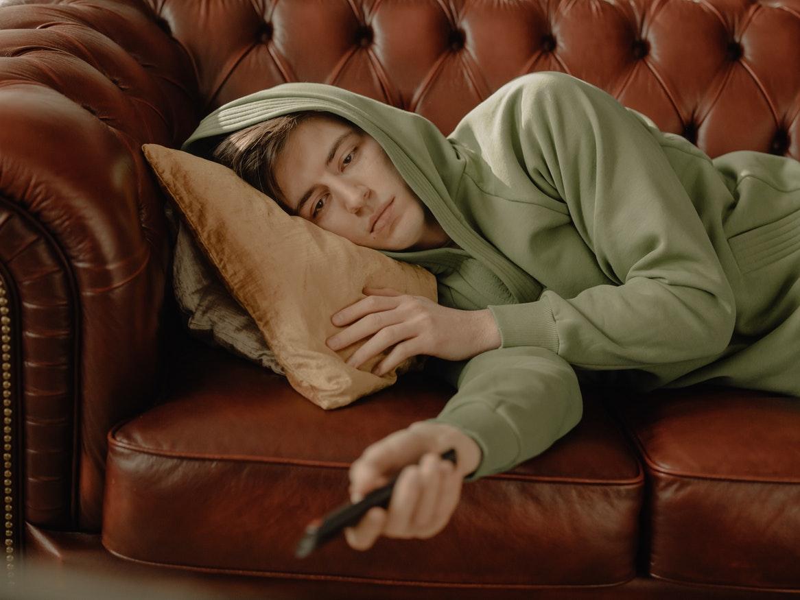 Young man in a green jumper on a leather couch using a remote controller