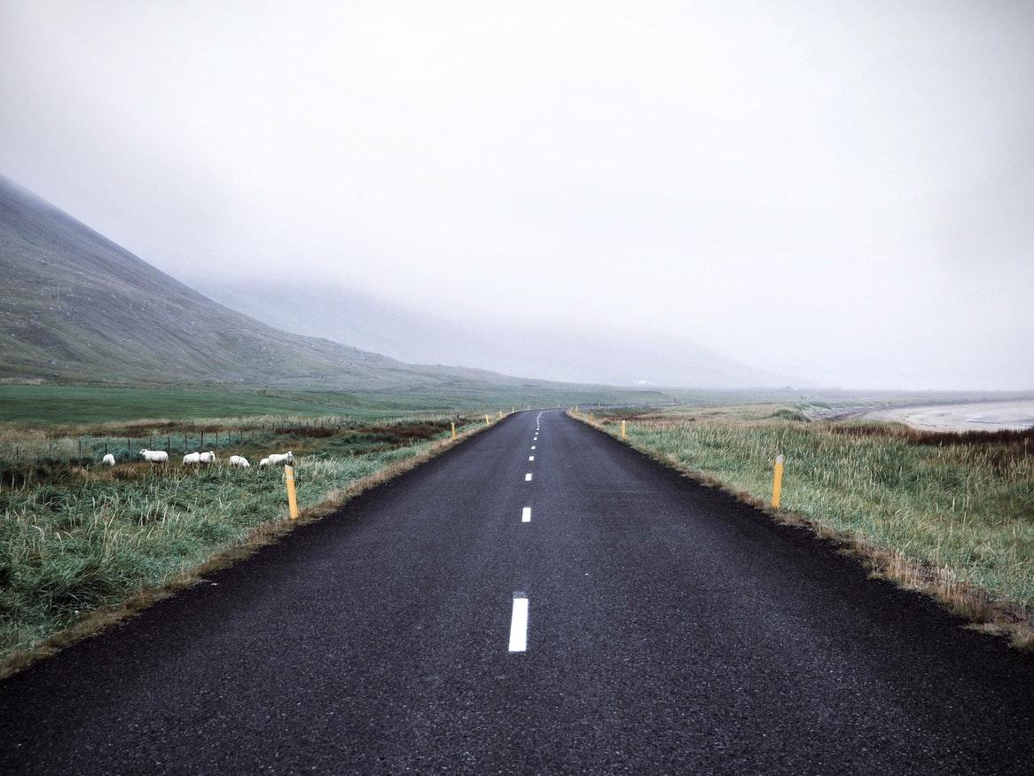 A foggy landscape with a long, black road stretching far in the distance.