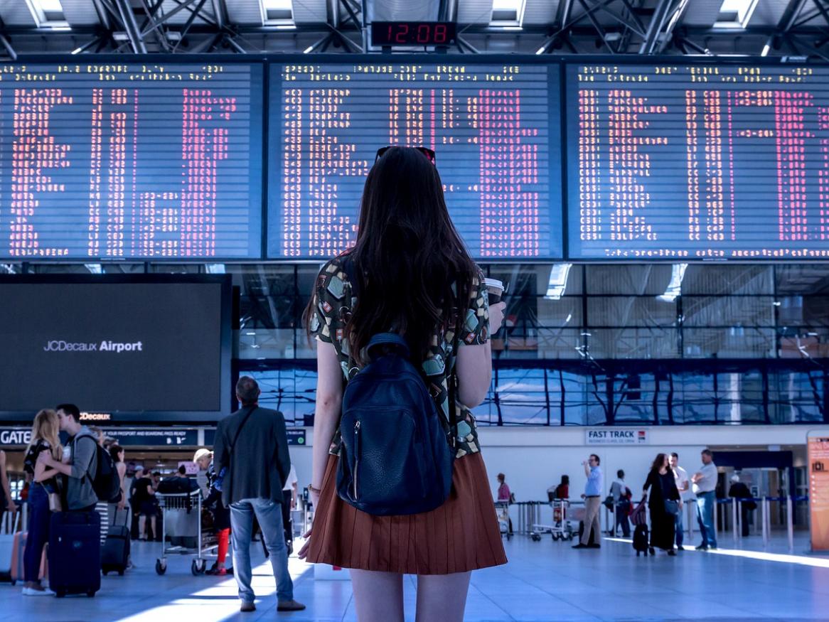 The back of a person at a busy airport, looking at the departures table