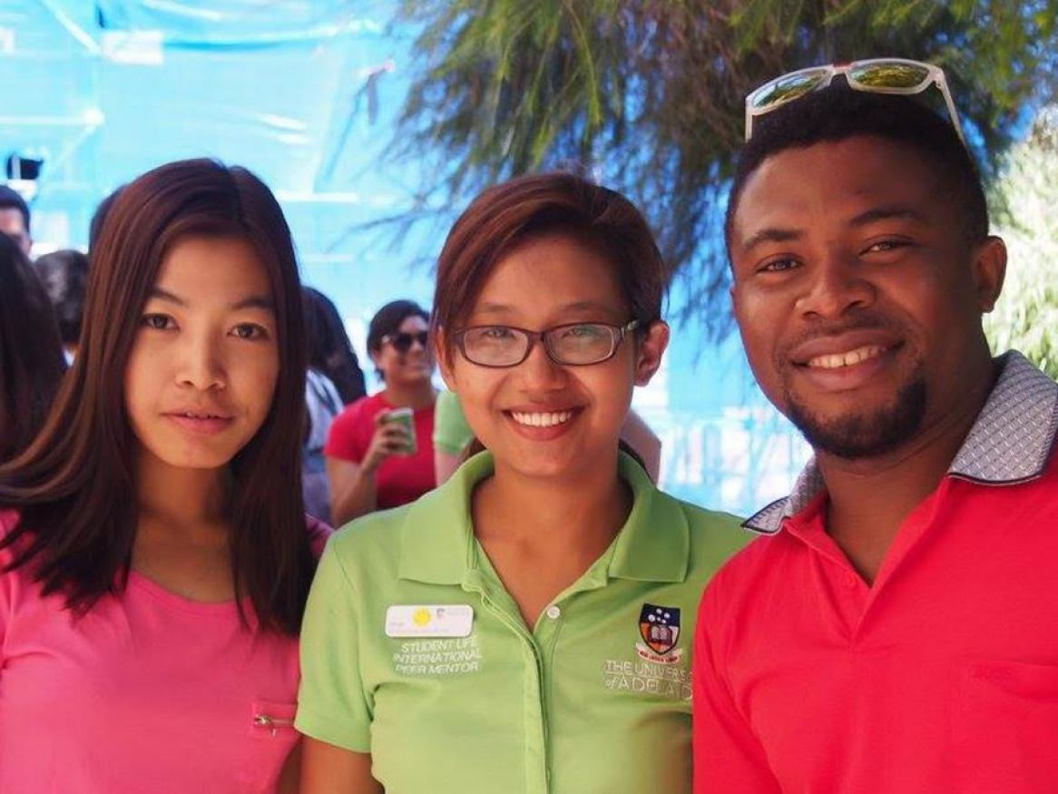 Photo of 3 people smiling at the camera wearing red, pink and green tshirts respectively