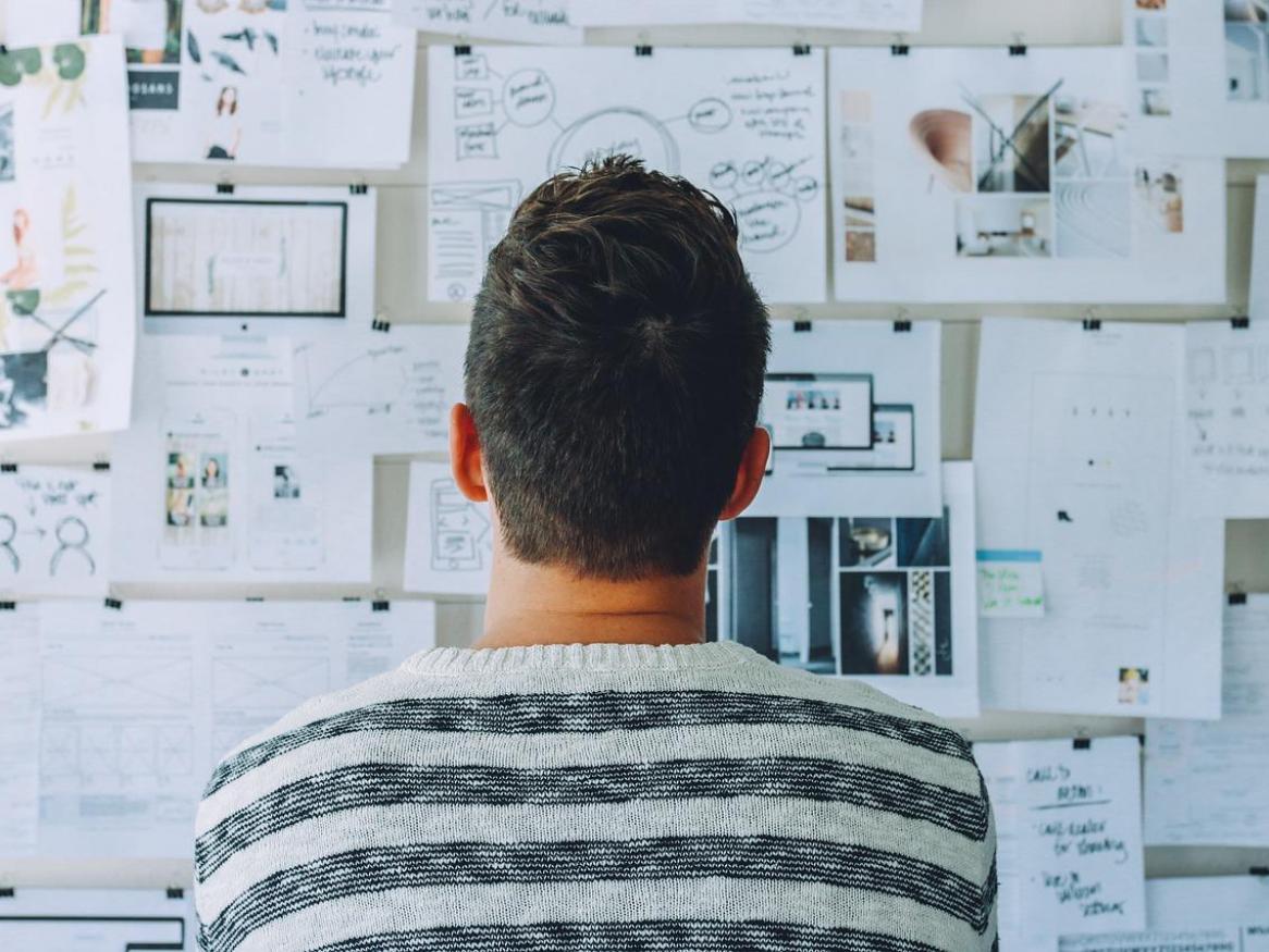 the back of a person who is looking at a wall filled with papers of ideas, concepts, and plans.