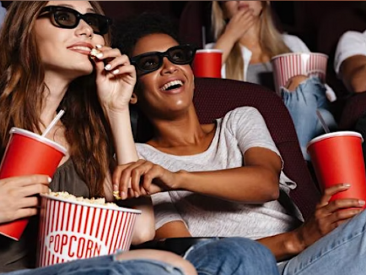 2 people sitting with popcorn looking at a movie screen