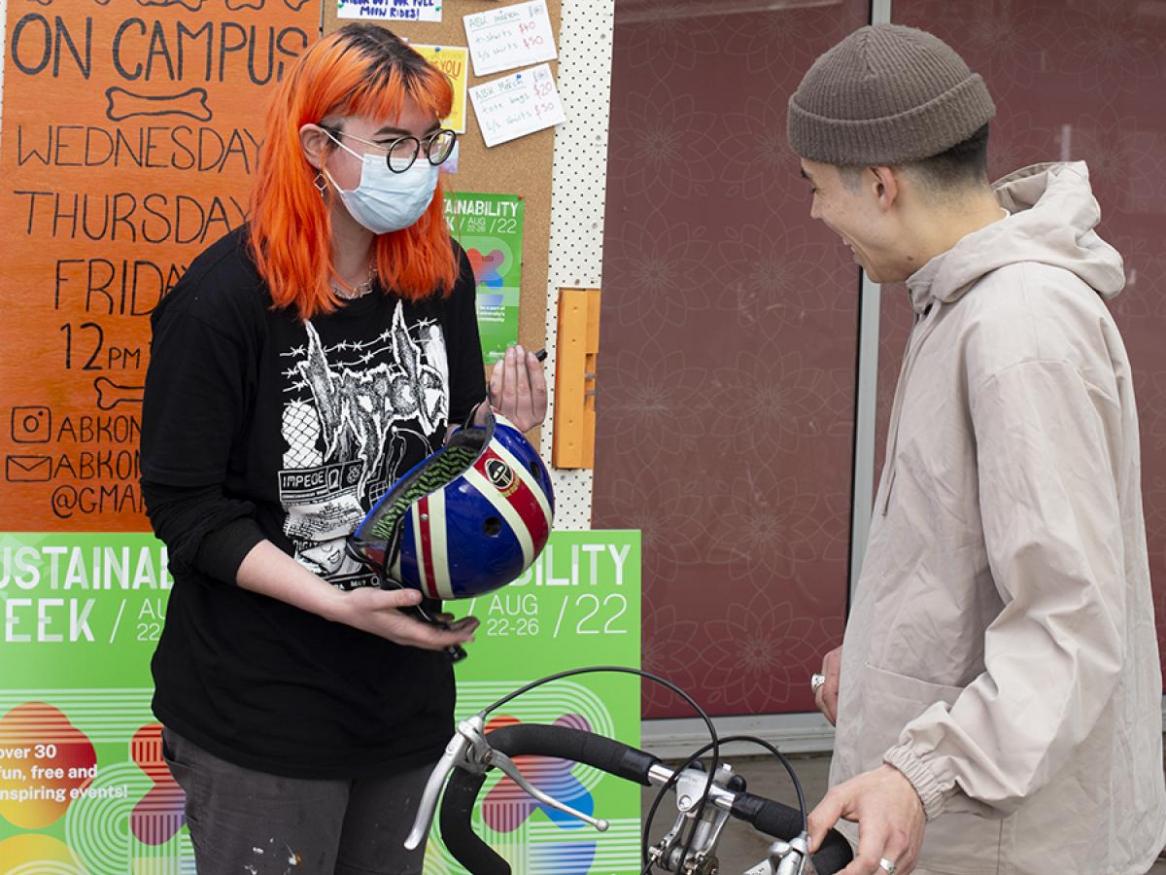 2 people looking at each other, bike in between, one holding a helmet and wearing a mask