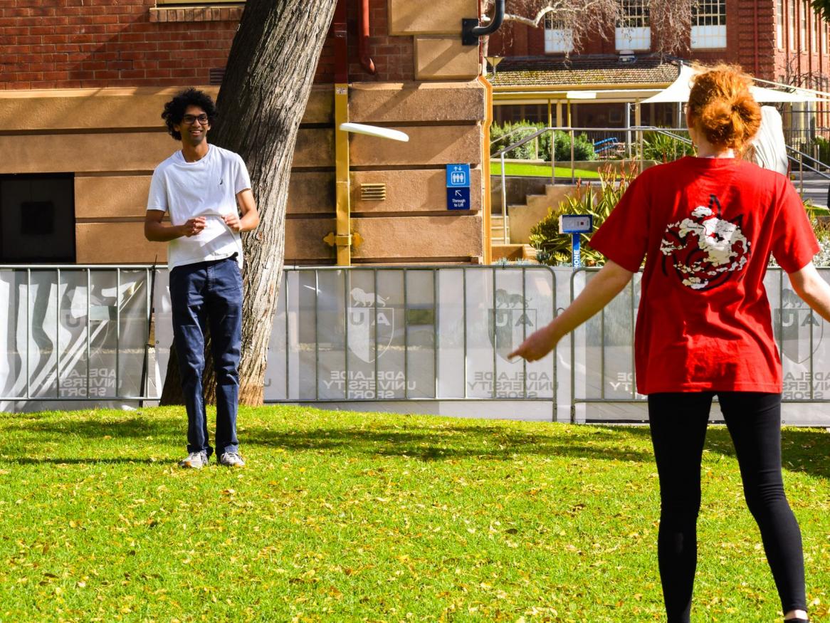 Photo of 2 people playing frisbee, one wearing a red tshirt, one wearing a white tshirt