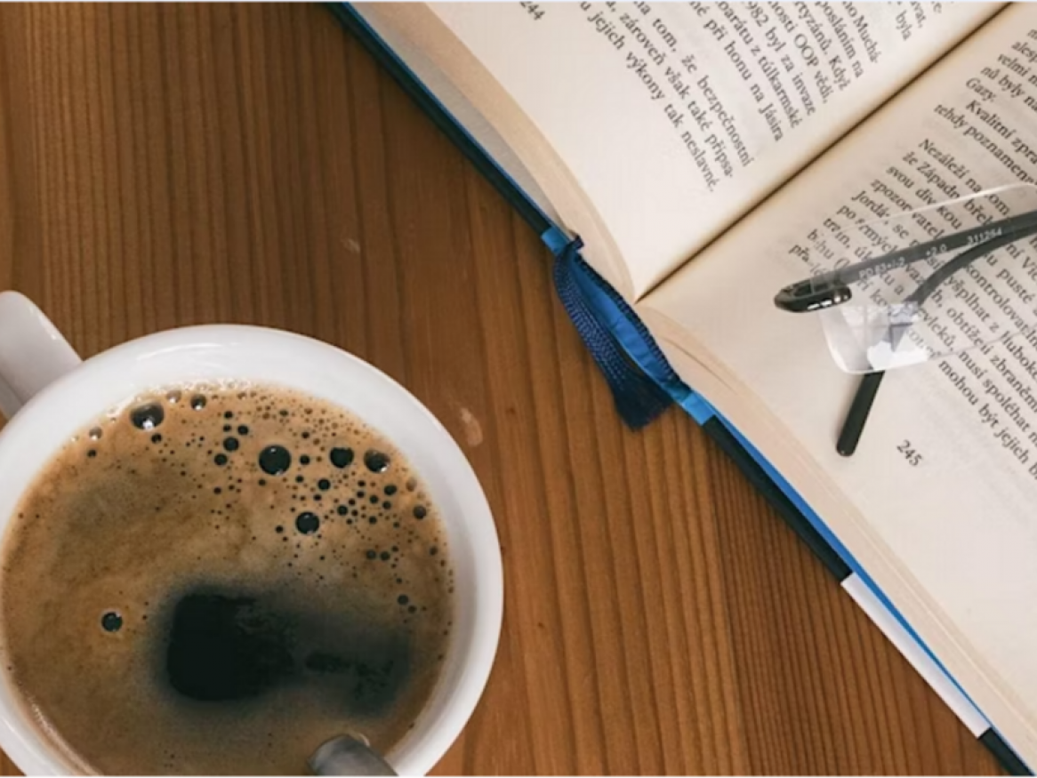 Photo of a cup of coffee from above, book and glasses
